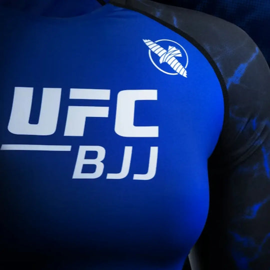 Close-up van het witte UFC BJJ-logo op de borst van de blauwe rashguard. De print is strak, helder en goed zichtbaar op het gladde stretchmateriaal. De omliggende zwarte en blauwe panelen versterken het sportieve ontwerp.