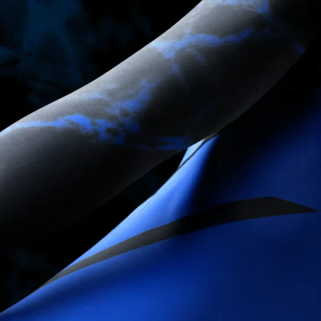 Close-up van de mouw van de zwarte-blauwe UFC BJJ Women’s Rashguard, met een opvallend blauw marmerpatroon. De stretchstof volgt de contouren van de arm nauwkeurig en laat de kwaliteit van de print duidelijk zien. De donkere achtergrond versterkt het contrast en de premium uitstraling.