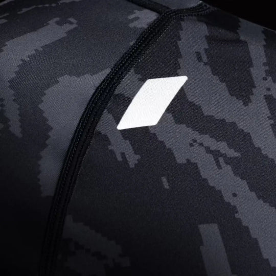 Close-up van zwarte rashguard met camo-patroon en wit geometrisch logo op de borst.
