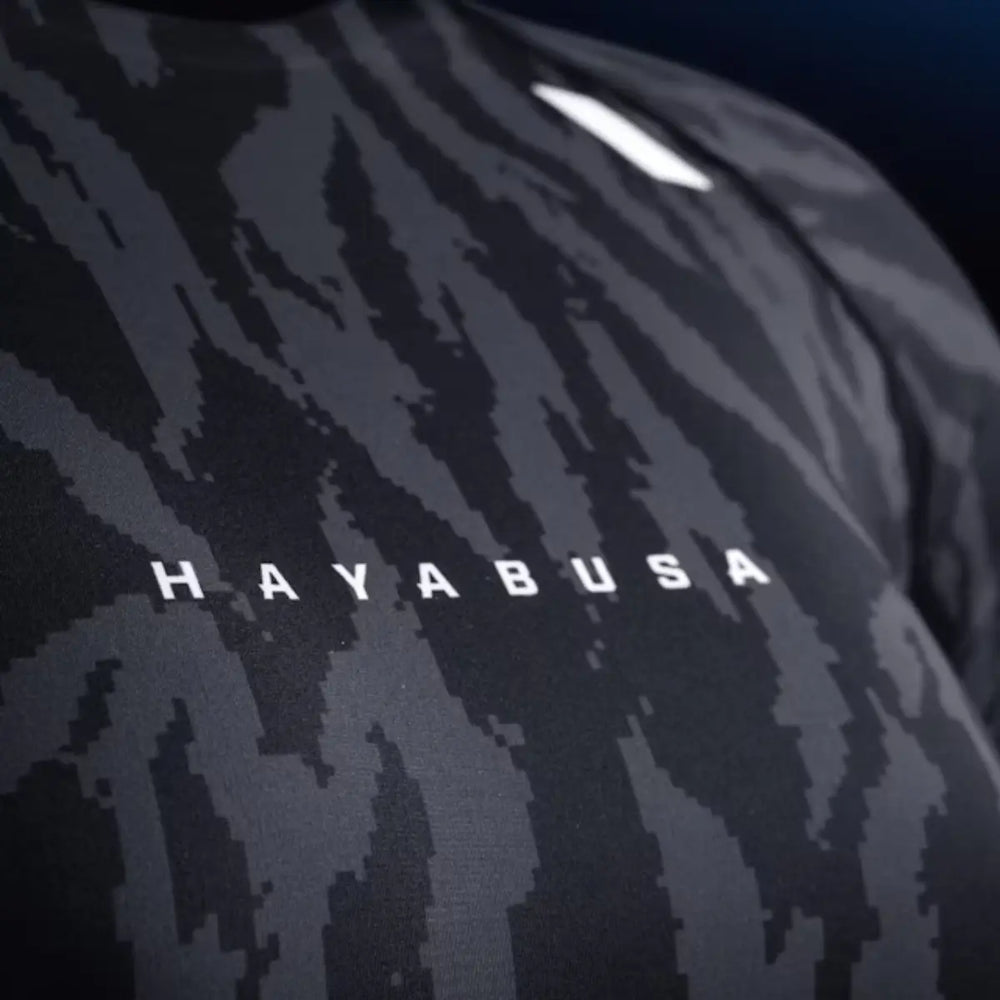 Close-up van zwarte Hayabusa rashguard met grijs camouflagedesign en wit Hayabusa logo op de borst.