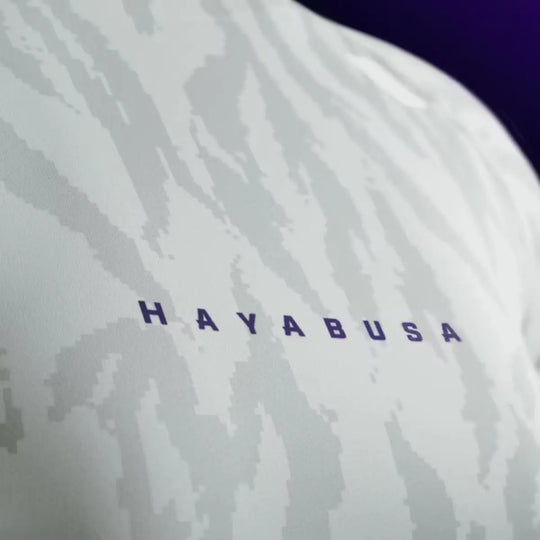 Close-up van het paarse Hayabusa logo op de borst van de witte rashguard met grijs camo-patroon.