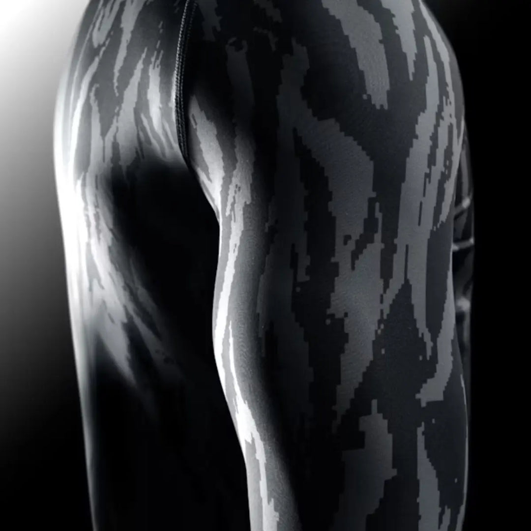Zijaanzicht van een arm en been, gekleed in strakke sportkleding met een pixelachtig, grijs camouflagepatroon.