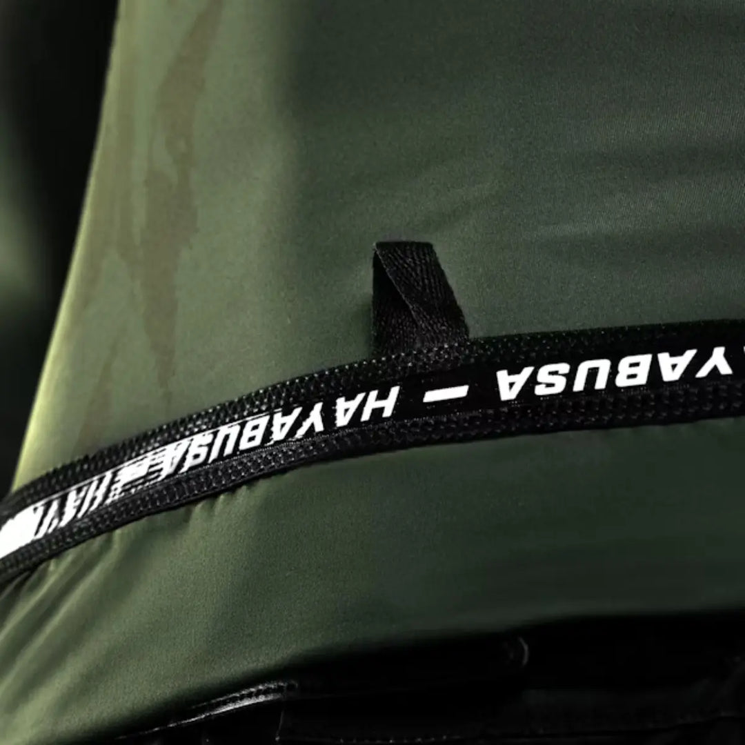 Detailopname van een donkergroen sportkledingstuk, met een zwarte band waarop het merklogo 'HAYABUSA' in witte letters staat.