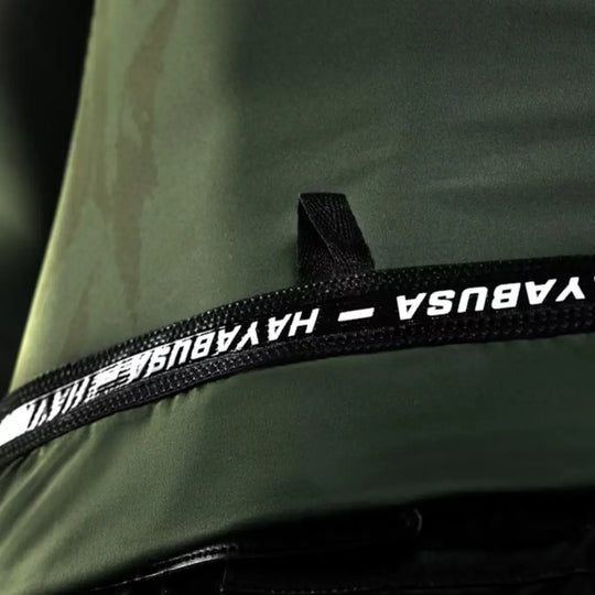Detailopname van een donkergroen sportkledingstuk, met een zwarte band waarop het merklogo 'HAYABUSA' in witte letters staat.