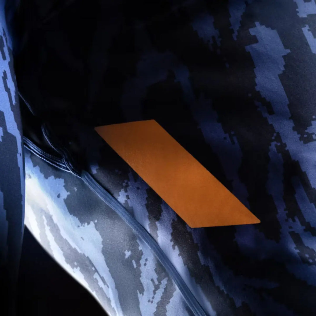 Close-up van de zijkant van een strak, donkerblauw sportshirt met een blauw, abstract pixelpatroon en een opvallend oranje paneel.