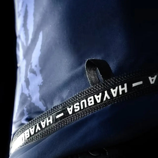 Detailopname van een donkerblauw sportshirt met een abstract blauw patroon en een zwarte, diagonale band met het witte 'HAYABUSA' logo.