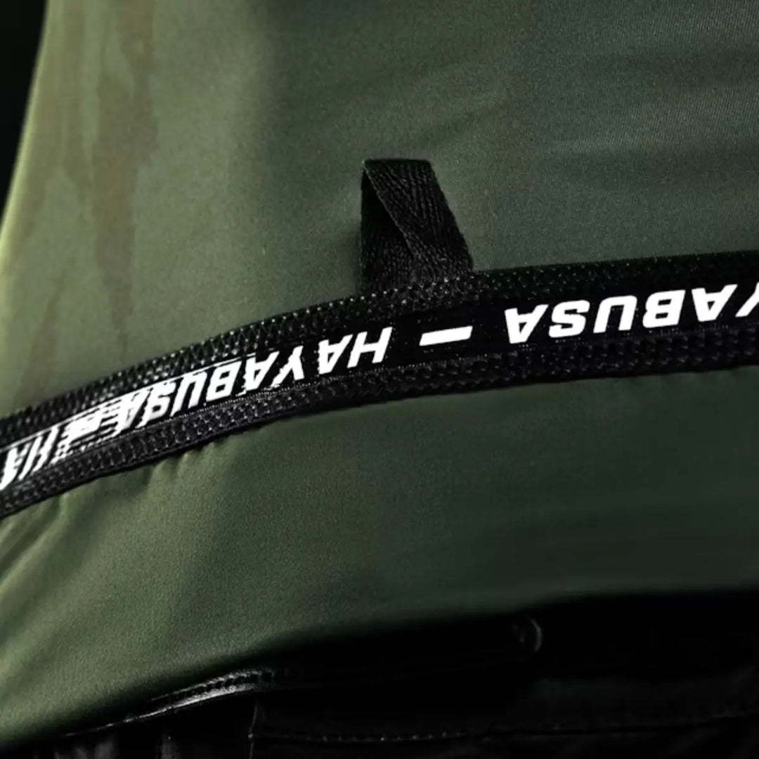 Detailopname van een donkergroen kledingstuk met een zwarte band die het 'HAYABUSA'-logo in witte letters toont.