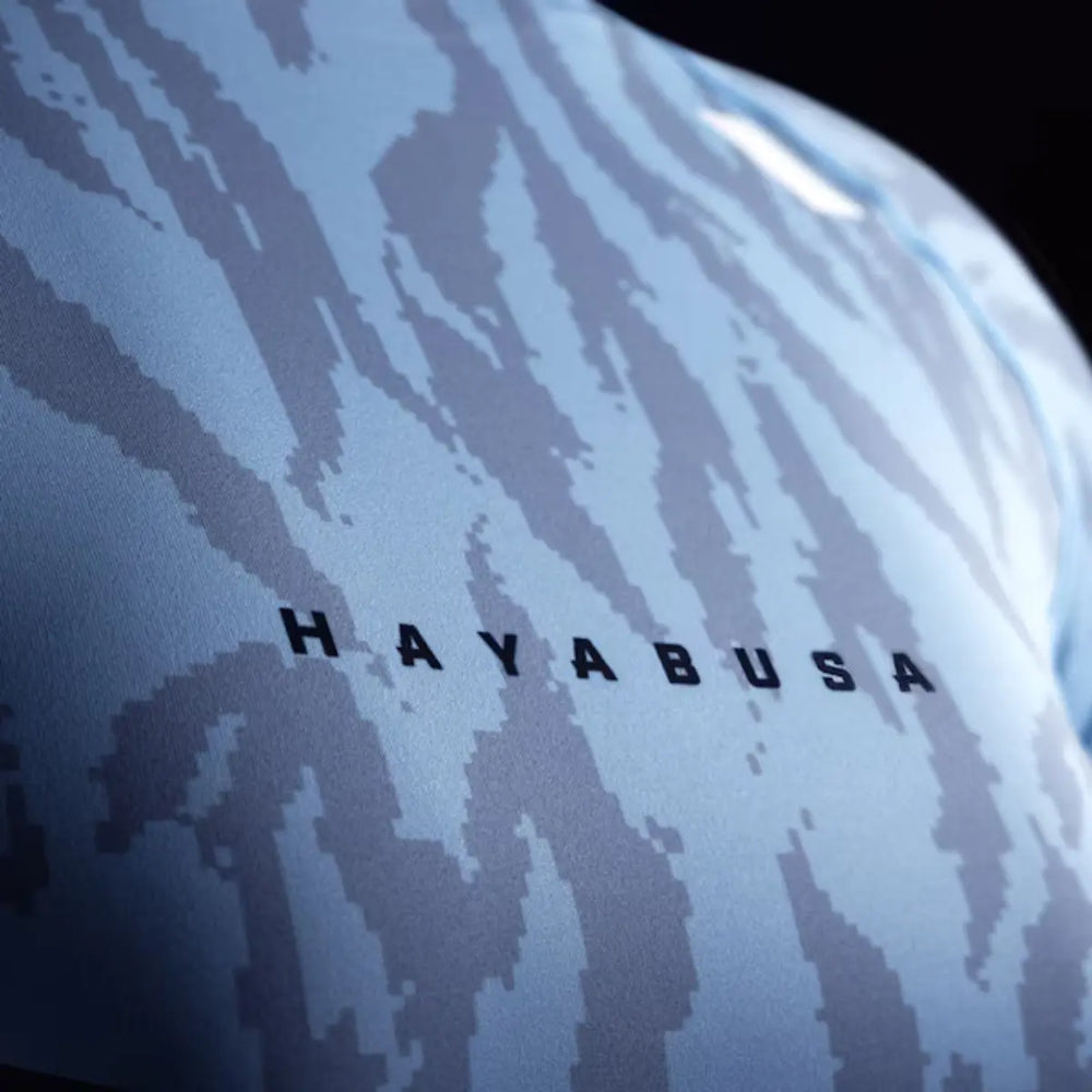 Close-up van de borst van de Hayabusa Apex dames rashguard korte mouw in Crystal Blue, met donkerblauw camo-patroon en zwart HAYABUSA-logo.