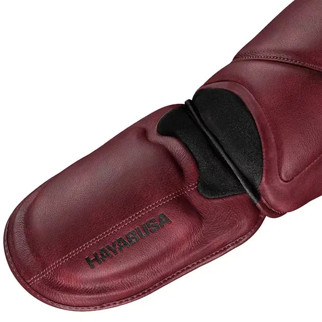 Close-up van het voetgedeelte van de Hayabusa T3 LX scheenbeschermer in crimson rood leer, met zwart logo en verstevigde afwerking voor maximale bescherming.