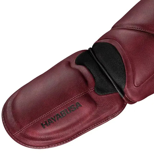 Close-up van het voetgedeelte van de Hayabusa T3 LX scheenbeschermer in crimson rood leer, met zwart logo en verstevigde afwerking voor maximale bescherming.