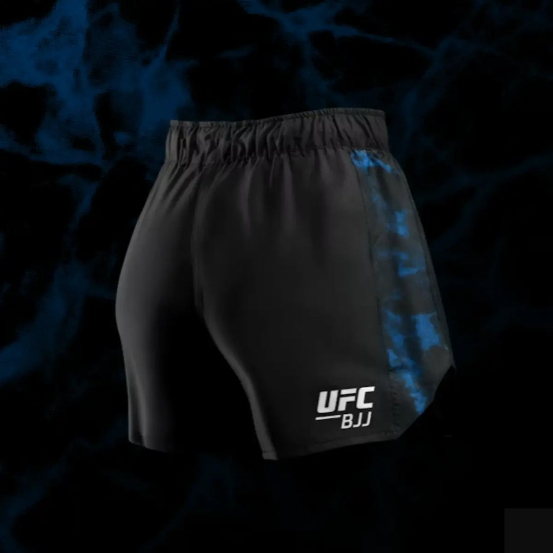 Deze afbeelding toont de achterkant van de zwarte UFC BJJ Women’s Shorts met blauwe zijpanelen. De stof valt strak en anatomisch gevormd voor bewegingsvrijheid. Het UFC BJJ-logo is duidelijk zichtbaar op de onderkant van het been. De achtergrond heeft een donkere, dynamische structuur die de sportieve uitstraling versterkt.