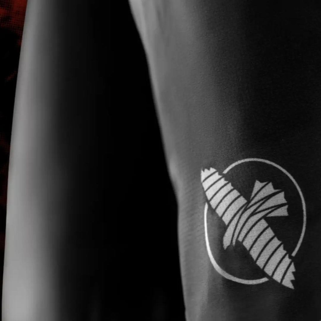 Detail van het witte pictogram op de shorts, afgebeeld op het zwarte textiel. De opdruk toont een gestileerd ontwerp dat scherp is gedrukt op de gladde stof. De foto legt de kwaliteit van het materiaal en de afwerking vast. De donkere achtergrond versterkt de focus op het logo.