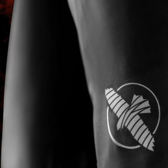 Detail van het witte pictogram op de shorts, afgebeeld op het zwarte textiel. De opdruk toont een gestileerd ontwerp dat scherp is gedrukt op de gladde stof. De foto legt de kwaliteit van het materiaal en de afwerking vast. De donkere achtergrond versterkt de focus op het logo.