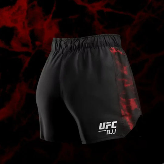 Achteraanzicht van de UFC BJJ Women’s Shorts in zwart met rode camouflage zijkanten. De pasvorm is anatomisch en sluit nauw aan voor optimale bewegingsvrijheid. Het UFC BJJ-logo is zichtbaar op het onderste deel van het been. De rode achtergrondstructuur geeft de foto een krachtige uitstraling.