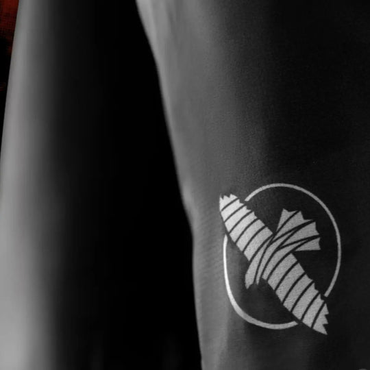 Detail van het witte pictogram op het zwarte been van de shorts. De opdruk is strak en duidelijk zichtbaar op de gladde stof. De afbeelding benadrukt de kwaliteit van de print en het materiaal. De donkere achtergrond zorgt voor extra contrast.