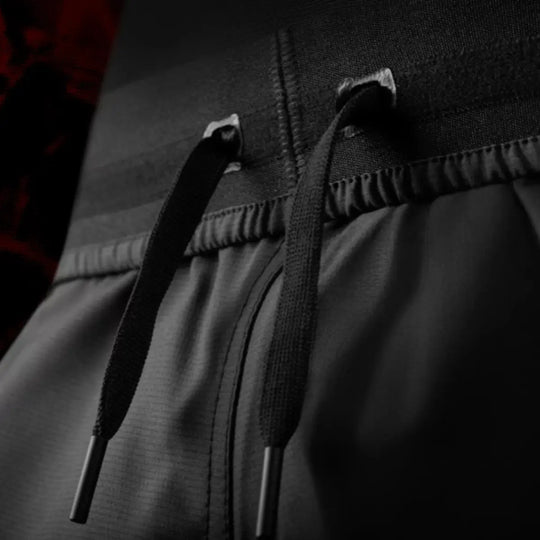Close-up van de vetersluiting aan de taille van de UFC BJJ Women’s Shorts. De zwarte koorden met stevige afwerking laten de verstelbare pasvorm zien. De elastische tailleband biedt stabiliteit tijdens beweging. De donkere sfeer geeft de foto een professionele uitstraling.