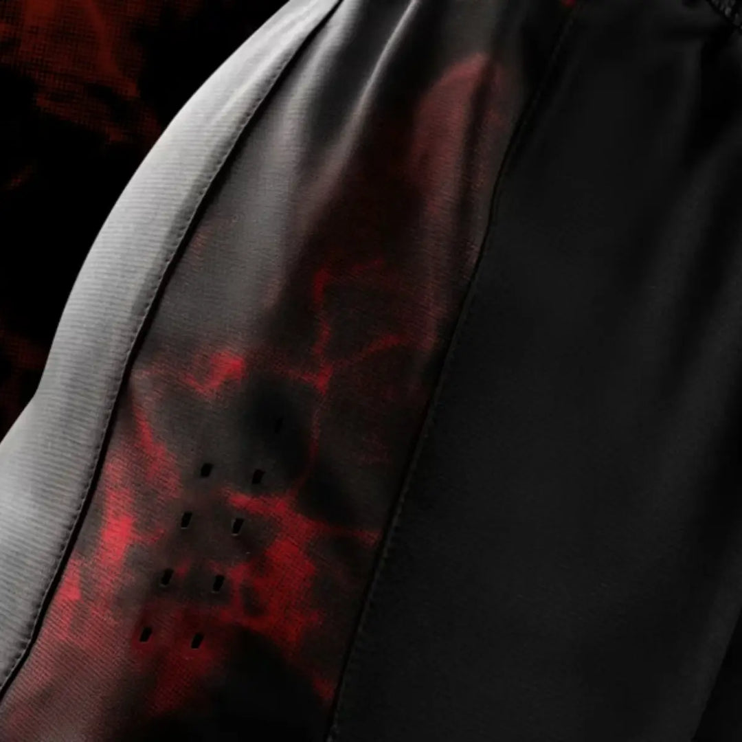 Detailfoto van het rode camouflagepaneel met ventilatiegaatjes aan de zijkant van de UFC BJJ Women’s Shorts. De textuur van het materiaal en de perforaties benadrukken ademend vermogen. Het zwarte middenpaneel contrasteert strak met het rode patroon. De donkere achtergrond versterkt de intensiteit van de kleuren.