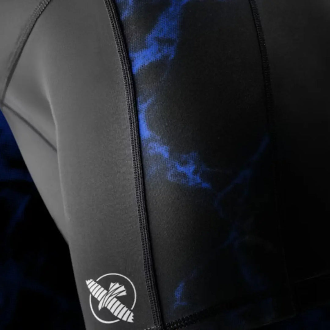 Close-up van het witte Hayabusa-pictogram op het been van de shorts. De gladde compressiestof en het stiksel komen duidelijk naar voren. Het blauwe marmeraccent naast het logo versterkt de dynamische look. De foto focust op de printkwaliteit en afwerking.