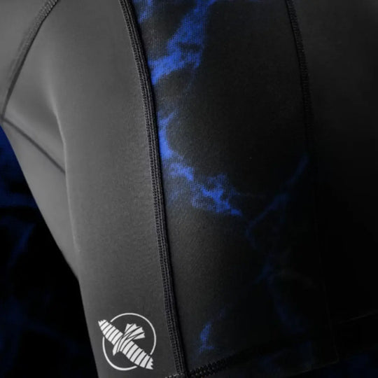 Close-up van het witte Hayabusa-pictogram op het been van de shorts. De gladde compressiestof en het stiksel komen duidelijk naar voren. Het blauwe marmeraccent naast het logo versterkt de dynamische look. De foto focust op de printkwaliteit en afwerking.