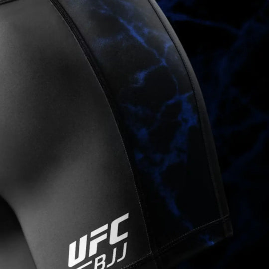 Detailfoto van het witte UFC BJJ-logo op de zwarte compressiestof. Het blauwe marmerpatroon aan de zijkant contrasteert scherp met het donkere materiaal. De foto benadrukt de kwaliteit van de print en de strakke anatomische pasvorm.