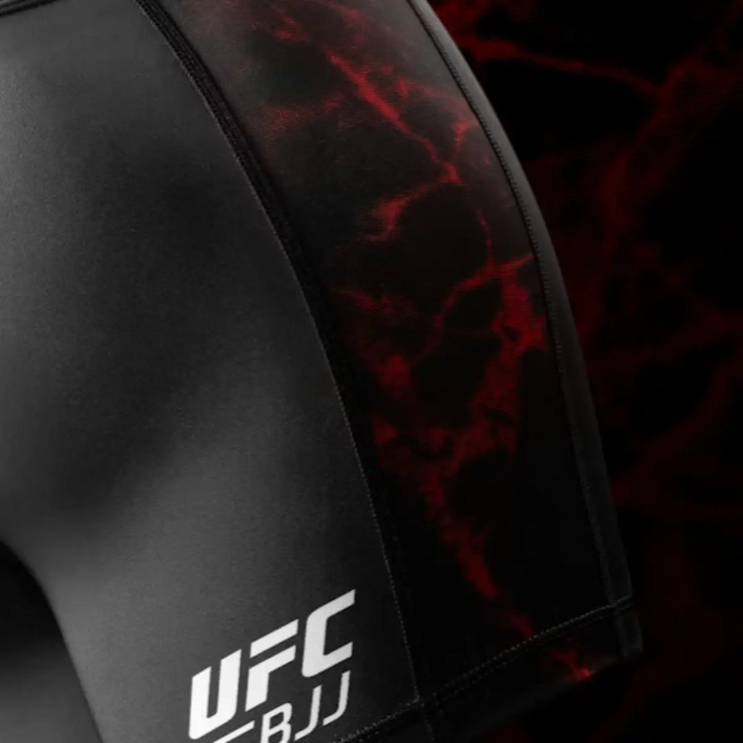 Close-up van het witte UFC BJJ logo op de zwarte Vale Tudo short met rood gemarmerde zijpanelen.