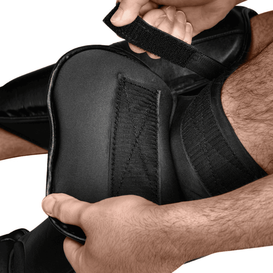 Close-up van een atleet die de klittenbandsluiting van een zwarte Hayabusa T3 Scheenbeschermer vastmaakt.