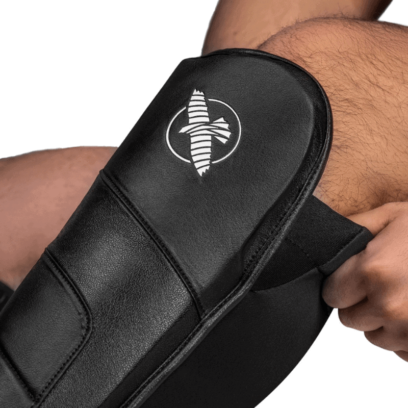 Close-up van het Hayabusa-logo op de zwarte T3 Full Back Scheenbeschermer die door een atleet wordt gedragen.