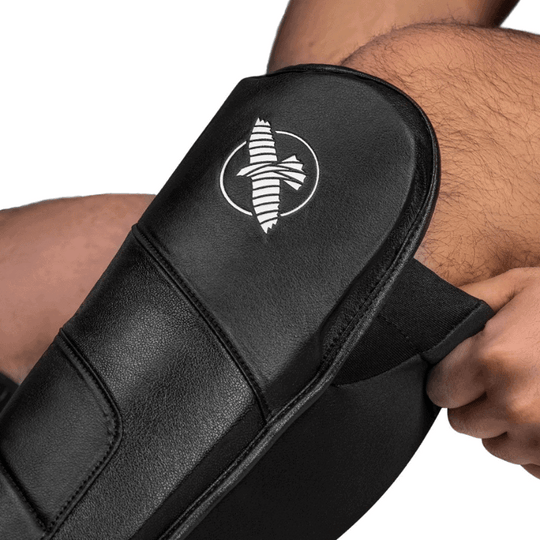 Close-up van het Hayabusa-logo op de zwarte T3 Full Back Scheenbeschermer die door een atleet wordt gedragen.