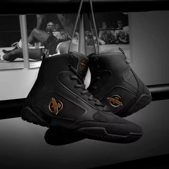 Zwarte Hayabusa boksschoenen hangend aan veters met gouden logo en rubberen zool.
