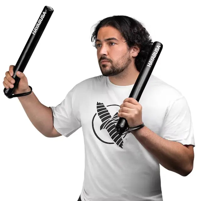 Man in wit T-shirt met vogelmotief houdt twee zwarte trainingssticks met het logo Hayabusa vast, witte achtergrond.