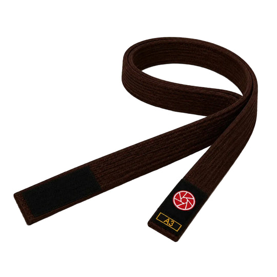 Bruine BJJ band in maat A3 met zwarte uiteinden en een rood-wit logo op het label. De stevige geweven structuur maakt de band geschikt voor BJJ-trainingen, graduaties en dagelijks gebruik op de mat.