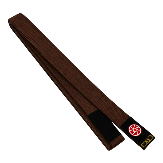 Bruine BJJ band in maat A3 met zwarte uiteinden en een rood-wit logo op het label. De lange, stevige geweven structuur maakt de band geschikt voor BJJ-trainingen, graduaties en dagelijks gebruik op de mat.