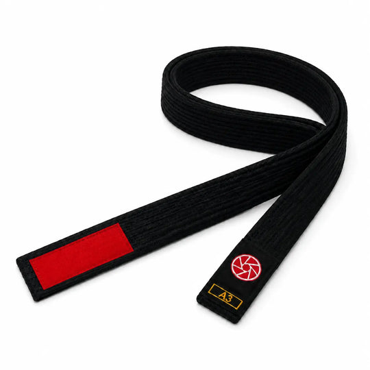 Zwarte BJJ band in maat A3 met rood vlak voor graduatiestrepen en een rood-wit logo op het label. De stevige geweven structuur maakt de band geschikt voor BJJ-trainingen, graduaties en dagelijks gebruik op de mat.