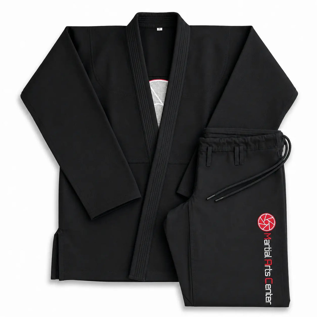Zwarte BJJ gi set met jas en broek, afgewerkt met een Martial Arts Center logo op de broekspijp. De stevige stof, klassieke pasvorm en verstelbare broeksluiting maken deze gi geschikt voor BJJ-trainingen, grappling en intensief gebruik op de mat.