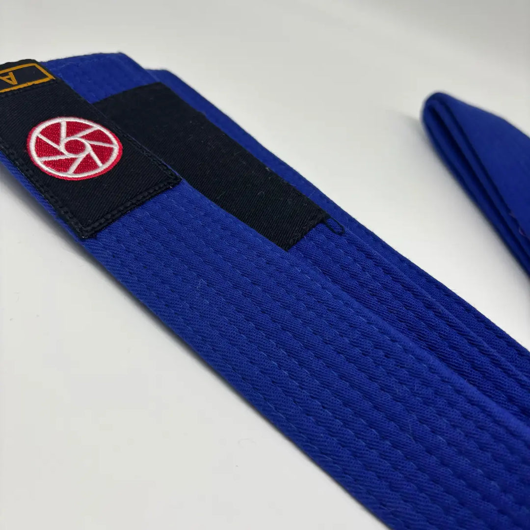Blauwe Martial Arts Center BJJ-band met zwart vlak en rood-wit patch op witte achtergrond, detailfoto van de band.