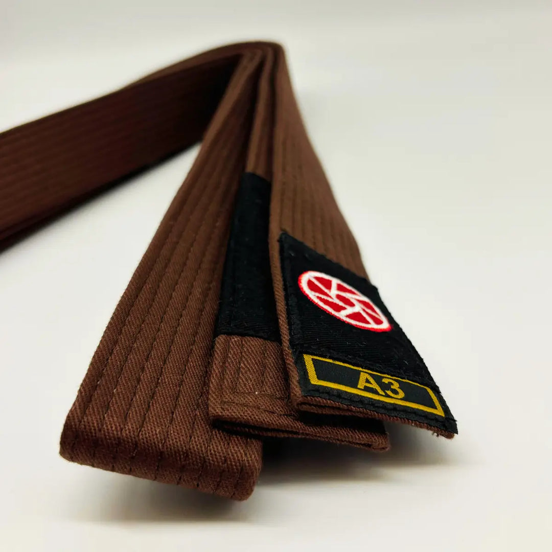 Bruine Martial Arts Center band met zwart label, rood rond logo en maatmarkering A3 op witte achtergrond.