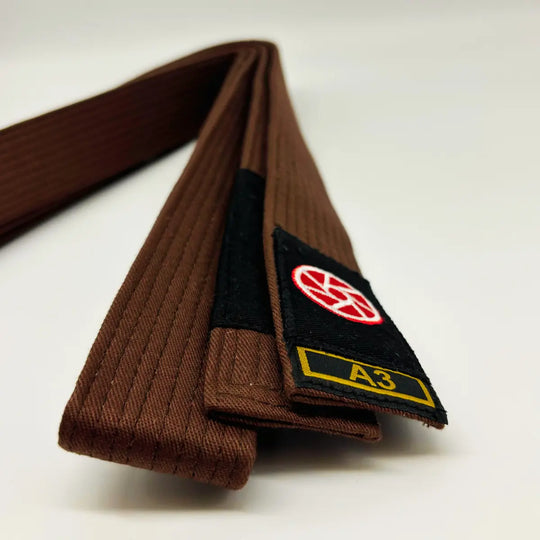 Bruine Martial Arts Center band met zwart label, rood rond logo en maatmarkering A3 op witte achtergrond.