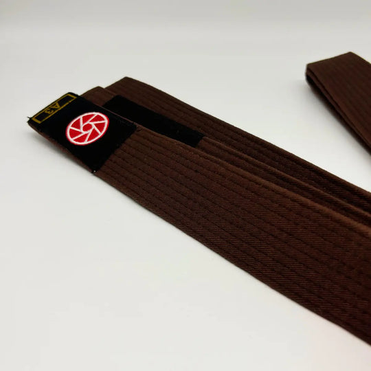 Bruine Martial Arts Center band met zwart label, rood rond logo en maatmarkering A3 op witte studioachtergrond.