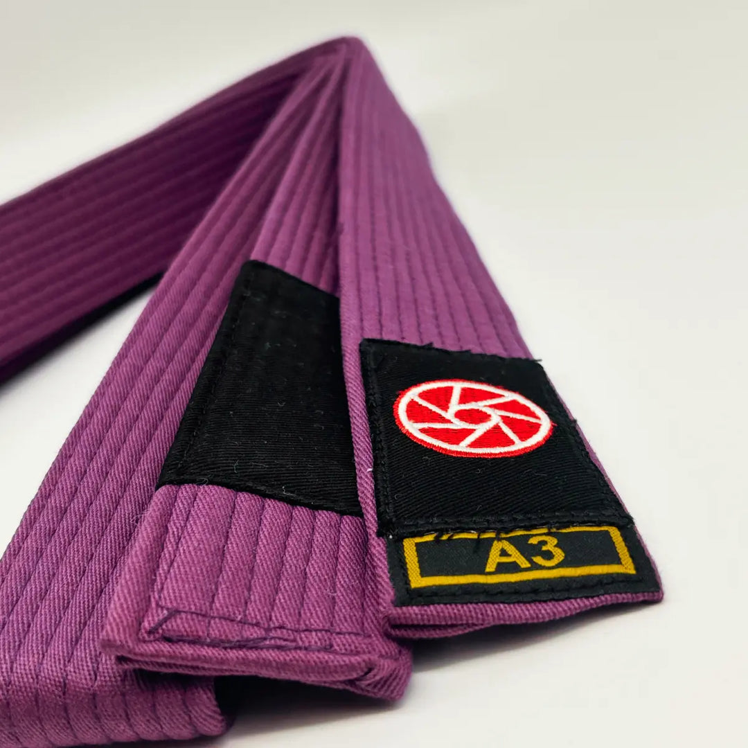 Paarse Martial Arts Center band met zwart label, rood rond logo en maatmarkering A3 op witte achtergrond.