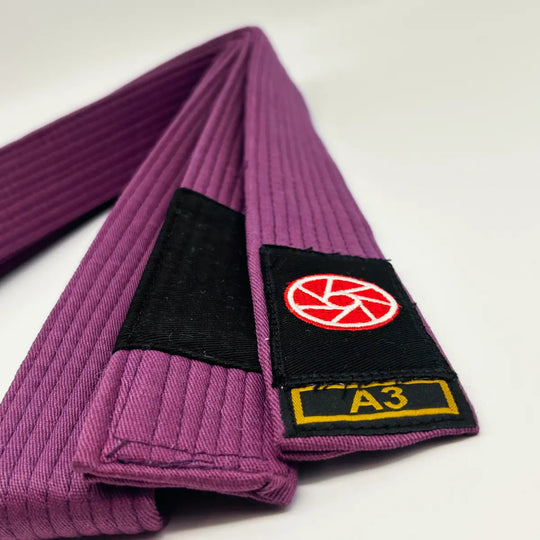 Paarse Martial Arts Center band met zwart label, rood rond logo en maatmarkering A3 op witte achtergrond.