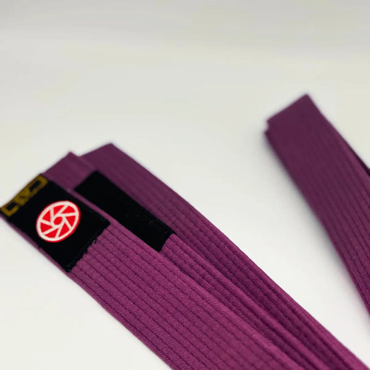 Close-up van paarse Martial Arts Center band met zwart label en rond rood logo op witte achtergrond.