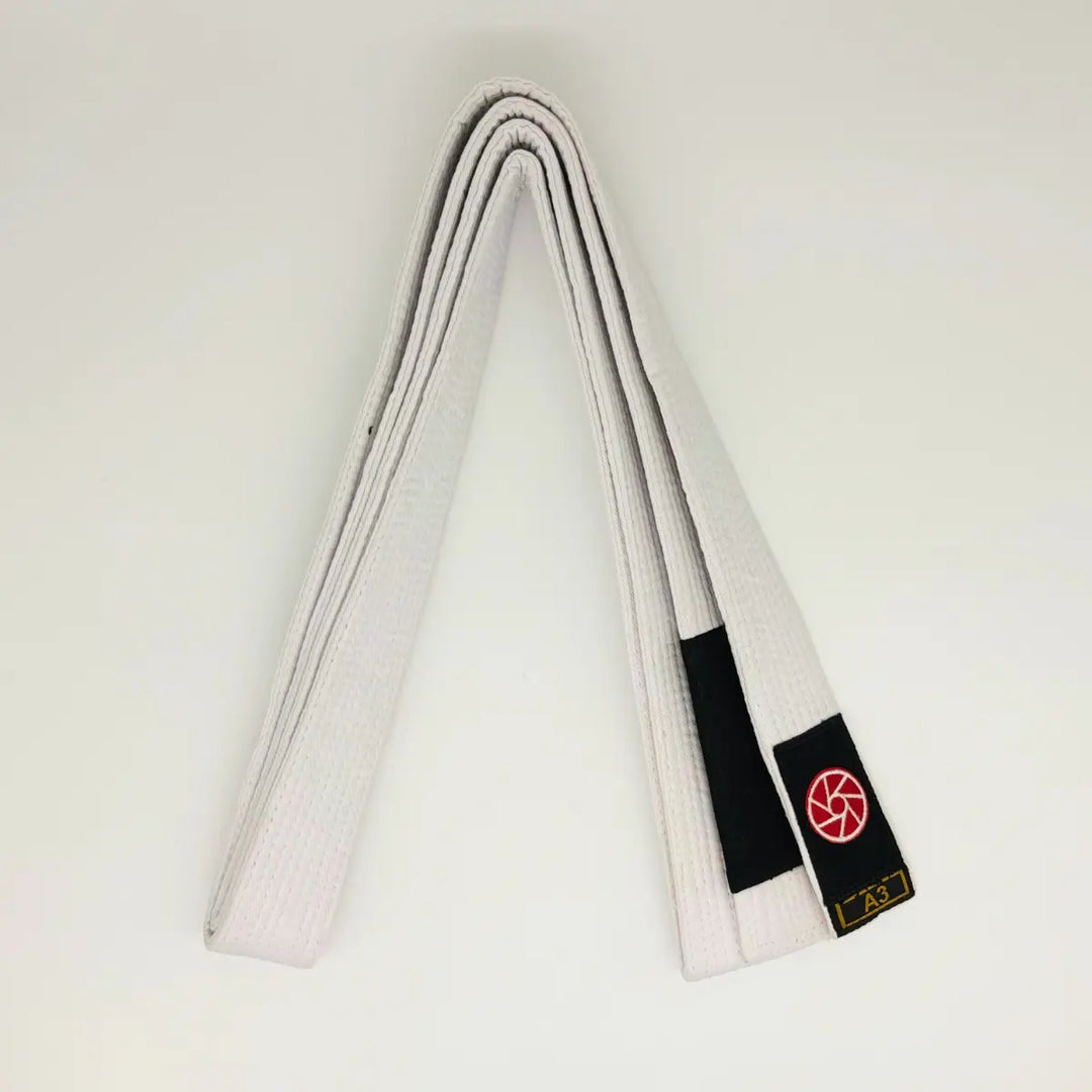 Witte Martial Arts Center band netjes opgevouwen met zwart label, rood rond logo en maatmarkering A3 op witte achtergrond.