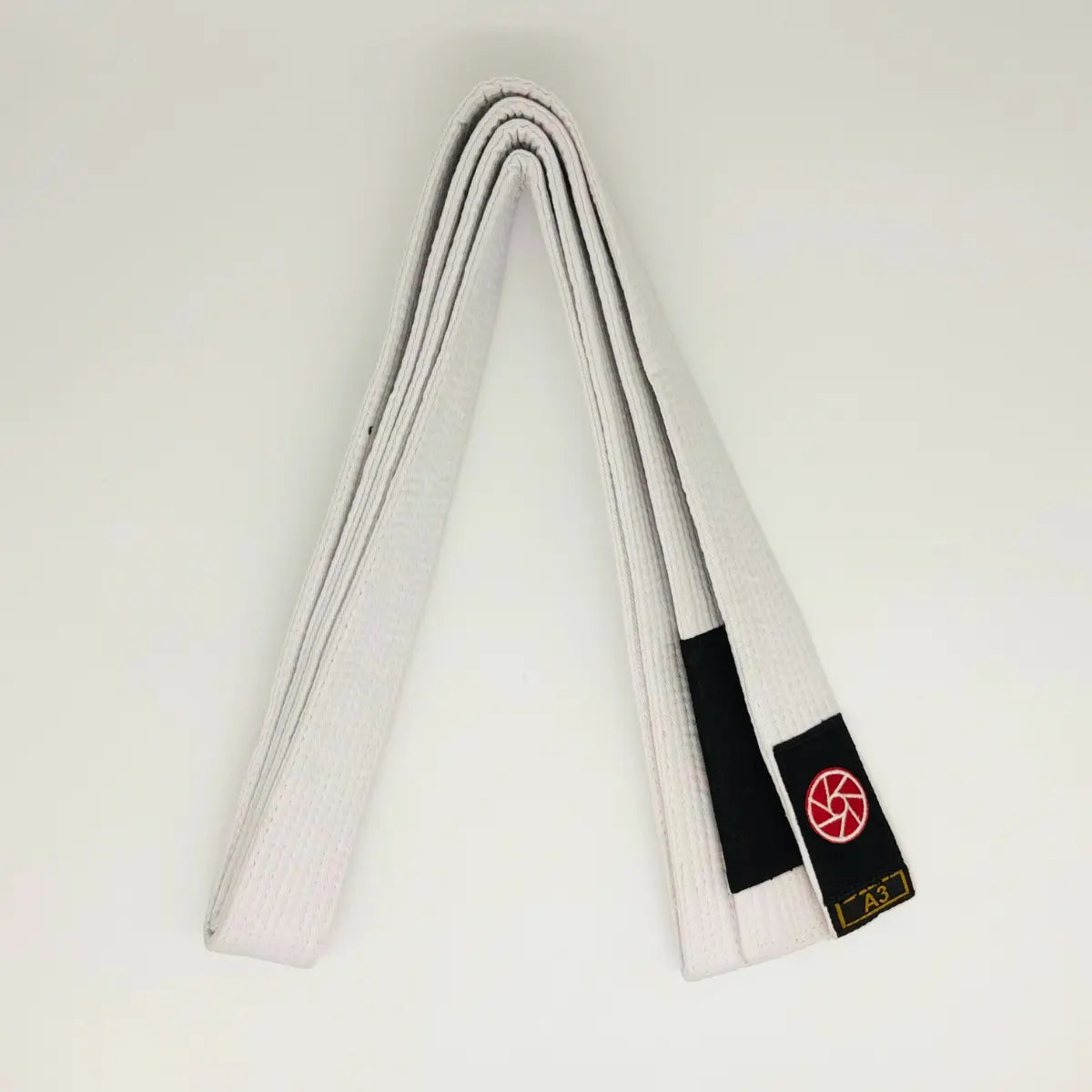 Witte Martial Arts Center band netjes opgevouwen met zwart label, rood rond logo en maatmarkering A3 op witte achtergrond.