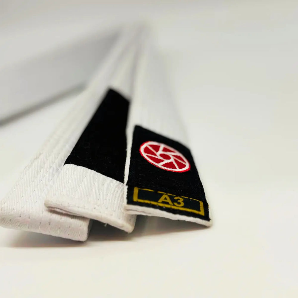 Witte Martial Arts Center BJJ band met zwarte gradenbalk en rood logo, maat A3, diagonaal in beeld op lichte achtergrond.