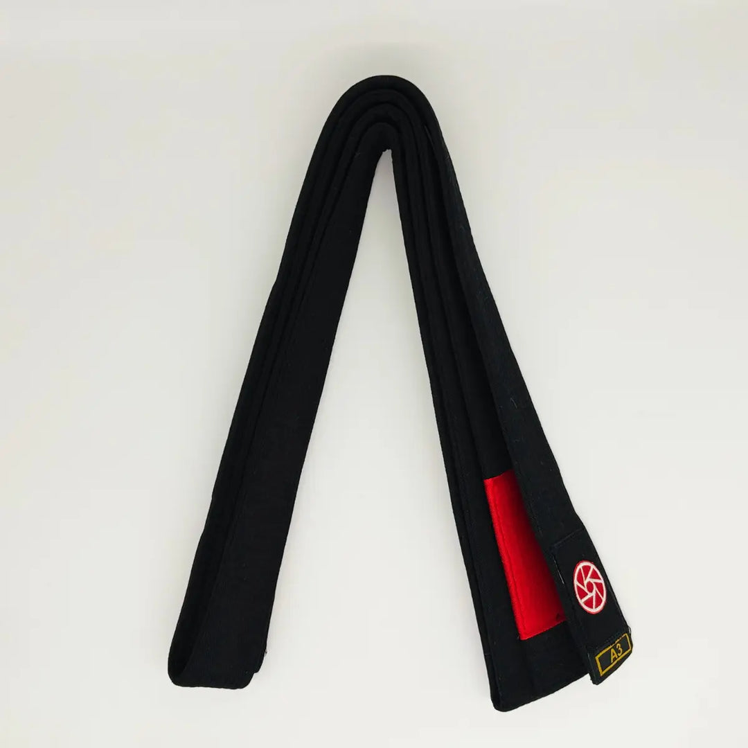 Zwarte Martial Arts Center band netjes opgevouwen met rood gradenstuk, rond rood logo en maatmarkering A3 op witte achtergrond.