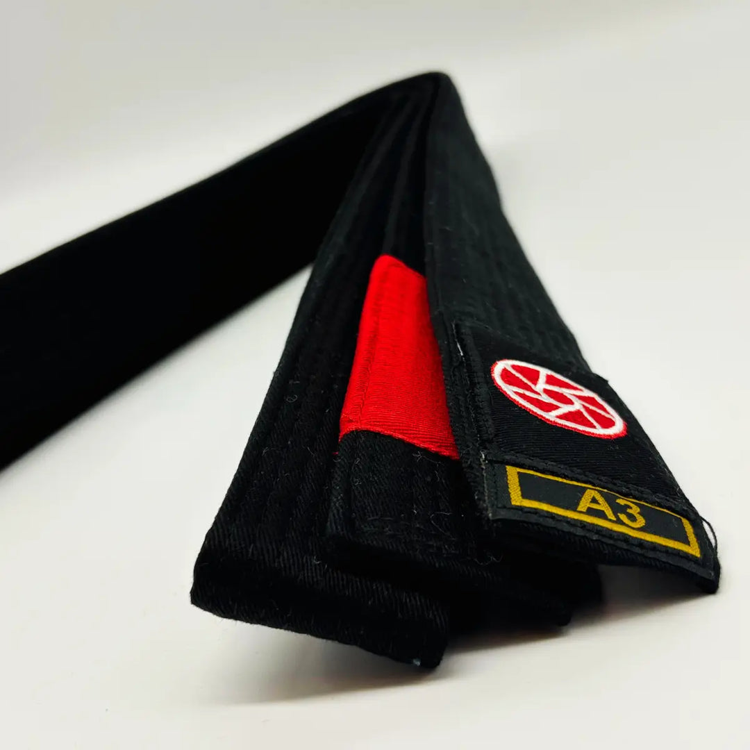 Zwarte BJJ-band maat A3 van Martial Arts Center met rood vlak en geborduurd logo, strak opgerold weergegeven op een witte achtergrond voor productweergave.