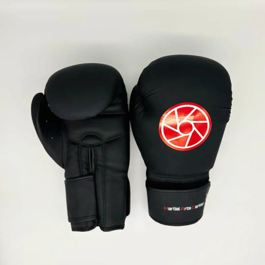 Bovenaanzicht van een paar zwarte Martial Arts Center bokshandschoenen met rood rond logo op de vuist en klittenbandsluiting bij de pols.