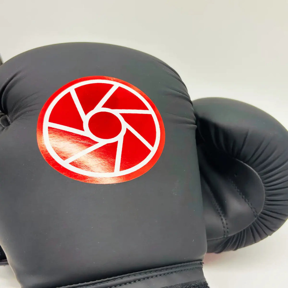 Close-up van zwarte Martial Arts Center bokshandschoen met groot rood rond logo op de bovenkant.