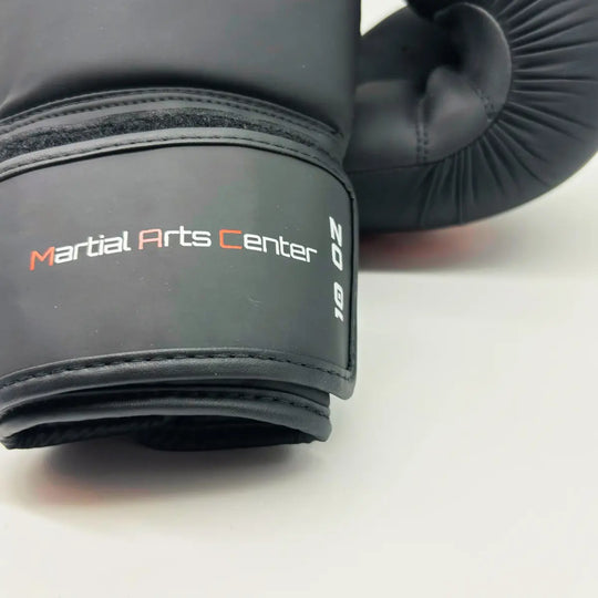 Close-up van zwarte Martial Arts Center bokshandschoen met klittenbandsluiting en wit-rood “Martial Arts Center” logo op de pols.