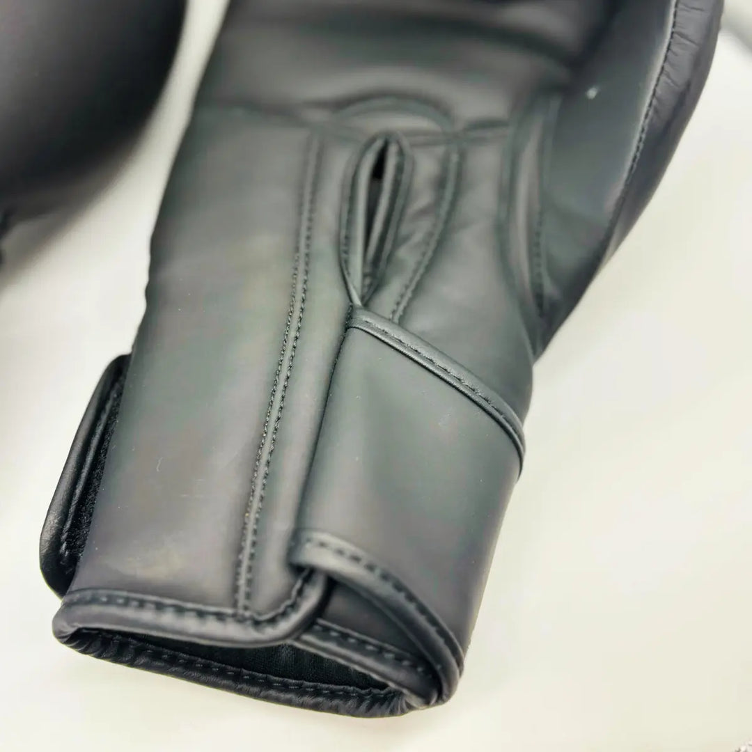Close-up van zwarte Martial Arts Center bokshandschoen met lange klittenbandsluiting en gladde palmzijde op witte achtergrond.